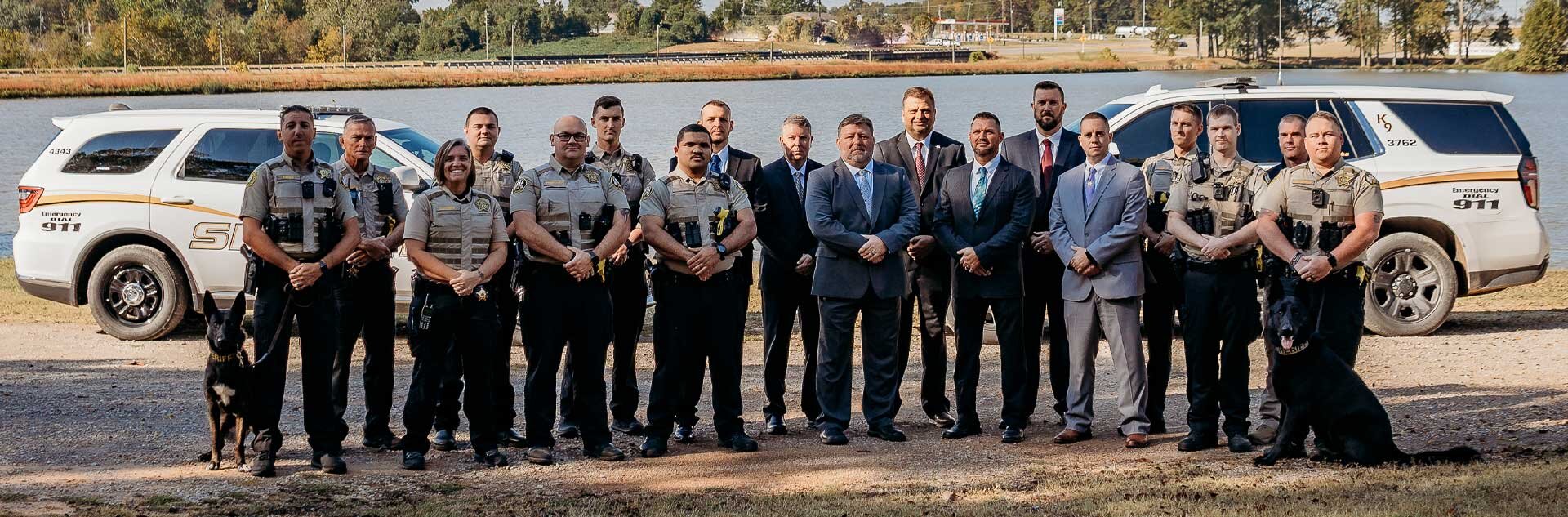 Sheriff's Office Staff and K9s standing in 2 rows in front of patrol vehicles